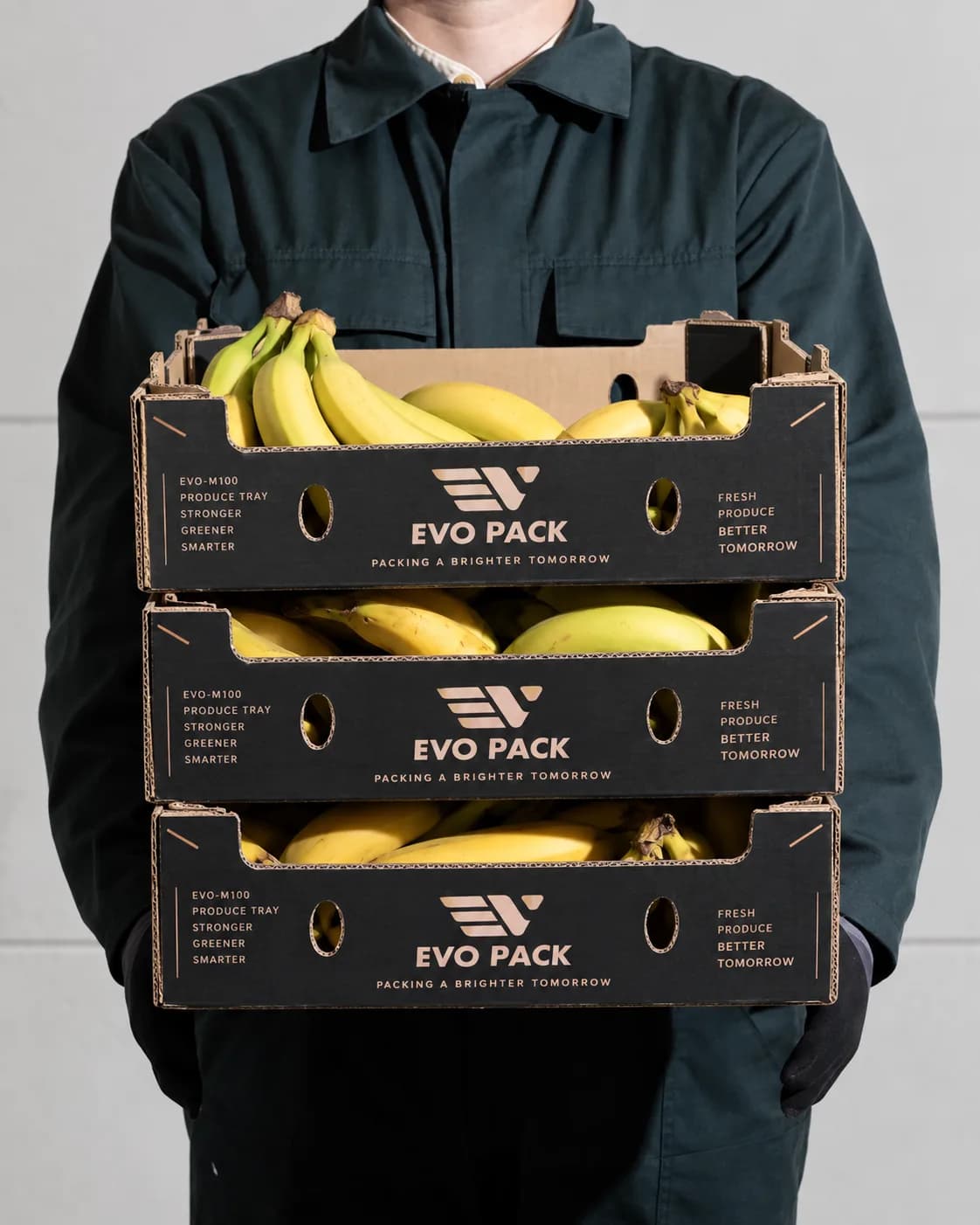 Worker carrying three stacked EVO PACK trays filled with bananas